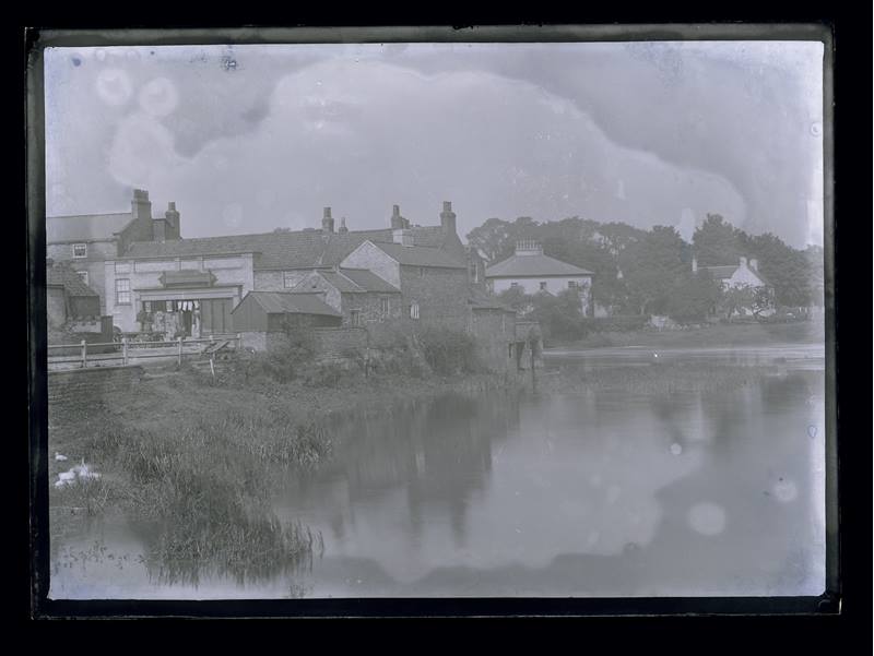 Unidentified group of houses on a river bank, c.1900