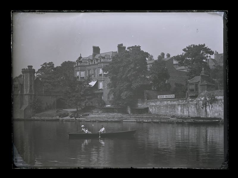 Couple boating on a river, with a large property in the background, c.1900